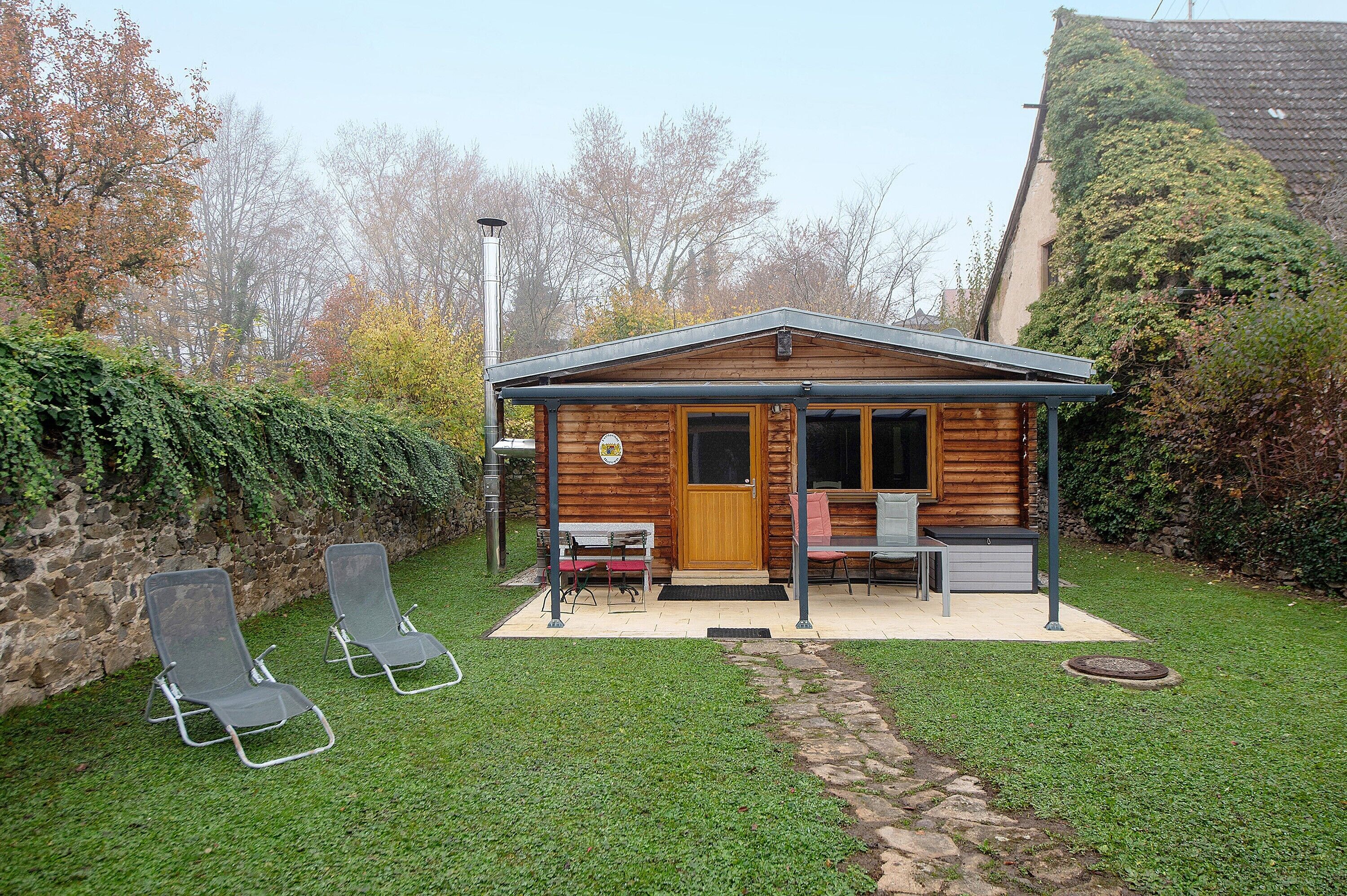 Eine Holzhütte mit Veranda, zwei Liegestühle, eine Bank und einem kleinen Tisch.