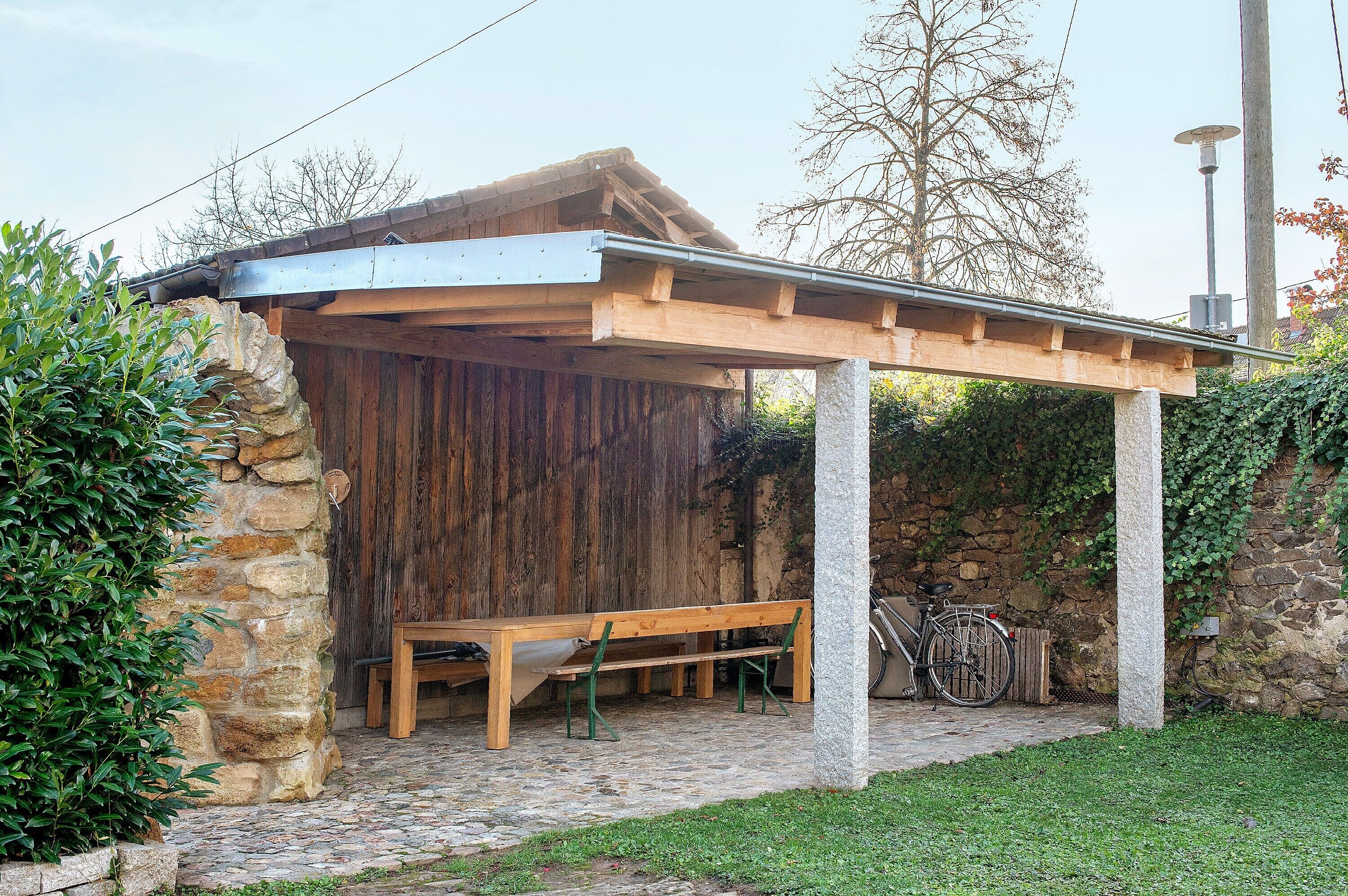 A covered outdoor seating area with a bench, a bicycle, and a stone wall.