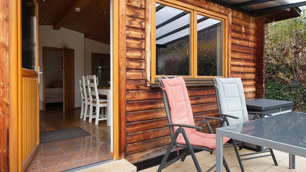 A wooden cabin with a patio area featuring a table and chairs, a door leading inside, and a window overlooking the outdoors.