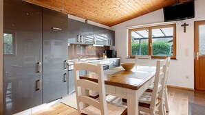 A modern kitchen with wooden ceiling, a dining table with chairs, and a large window with a view of greenery.