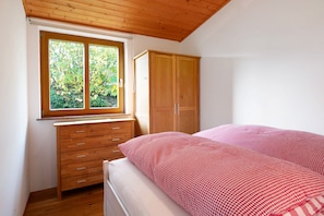 Un dormitorio con un armario de madera, una cama con colcha a cuadros, una ventana con vistas a la vegetación y un techo de madera.
