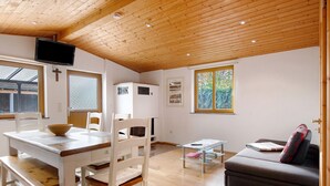 A room with a wooden ceiling, a dining table with chairs, a sofa, and a television mounted on the wall.