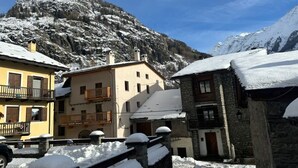 A snow-covered mountain village with traditional stone buildings and a prominent mountain in the background.