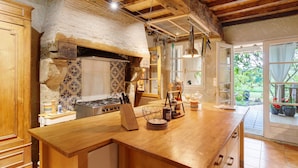 A kitchen with a wooden island, a stove, hanging utensils, and a view of the outdoors.
