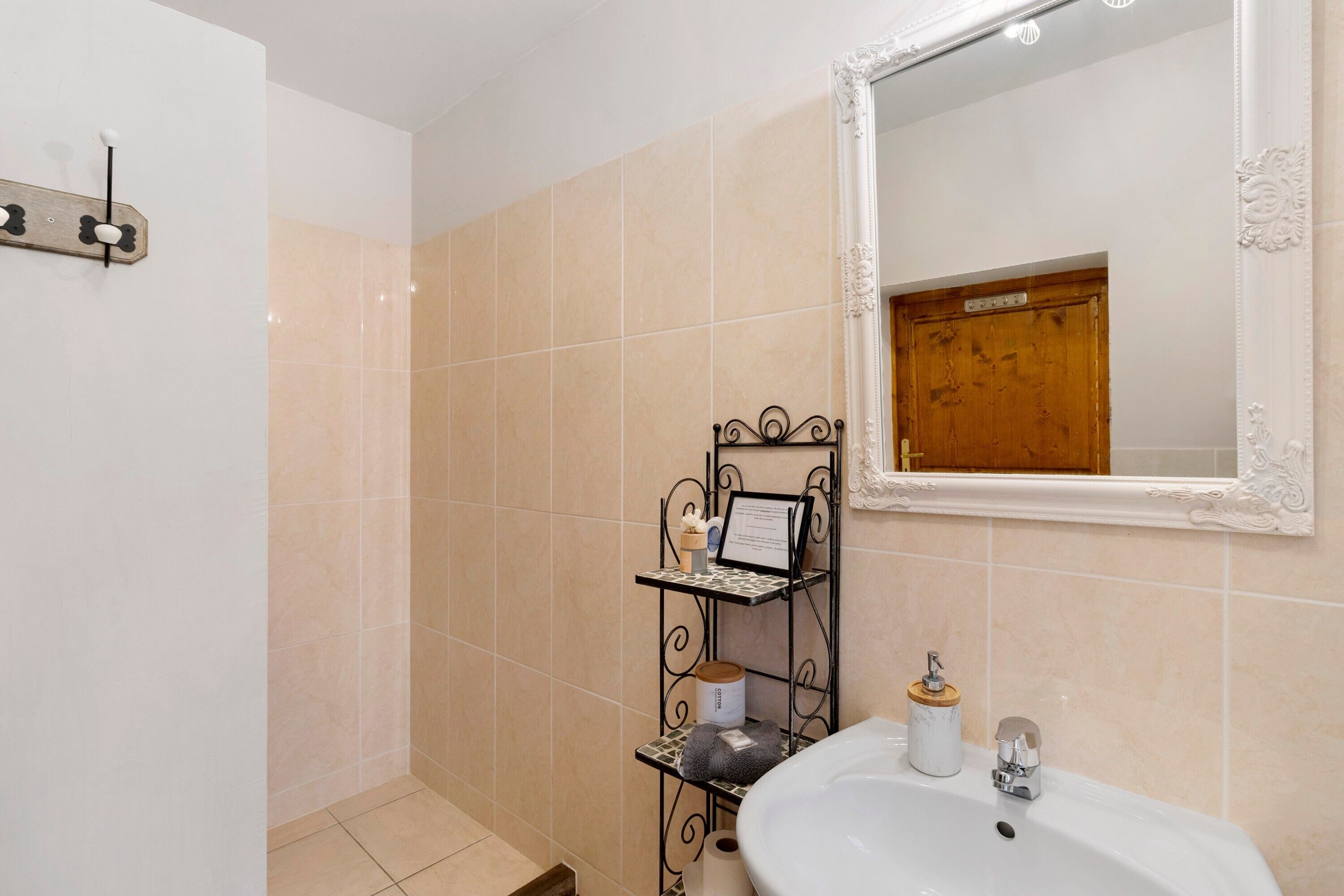 Une salle de bain avec un lavabo blanc, un miroir et une étagère en métal où sont rangés les articles de toilette.