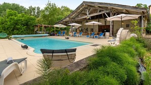 A pool area with lounge chairs, umbrellas, and a rustic building structure.