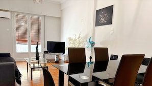 Una sala moderna con una mesa de comedor de vidrio, sillas negras, un sofá y un televisor.
