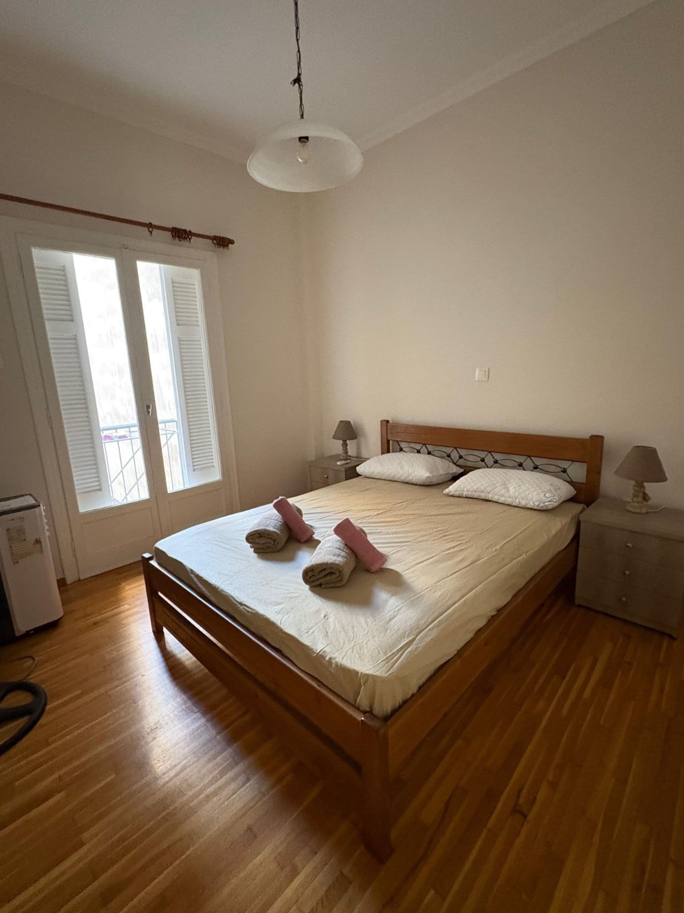 A bedroom with a wooden bed, two bedside lamps, a nightstand, and a window with shutters.