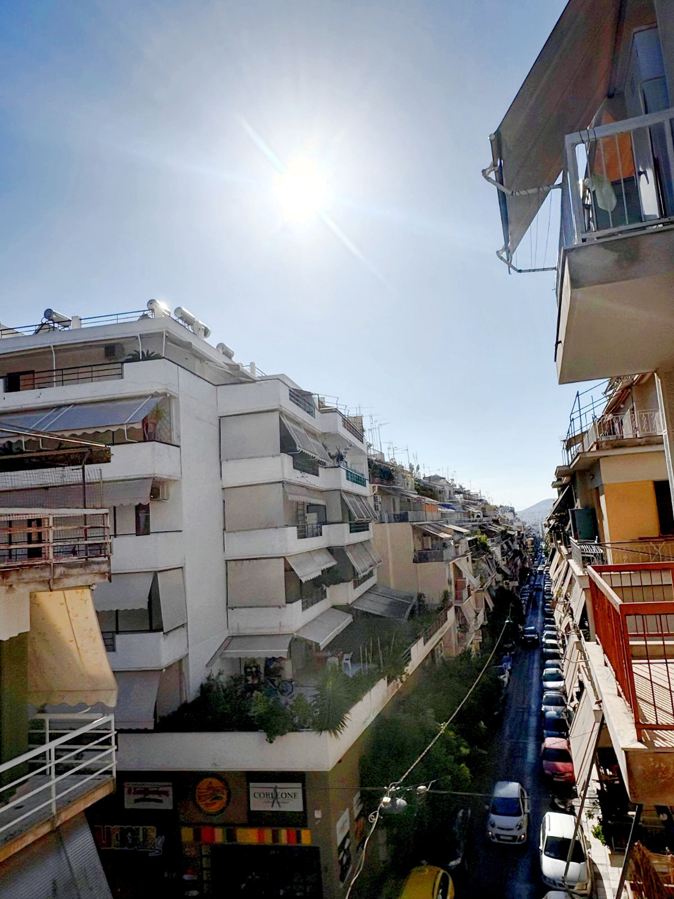 A multi-story residential building with balconies and a narrow street in the foreground.