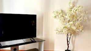 Un televisor de pantalla plana sobre un mueble de vidrio en una habitación con piso de madera y pared blanca.