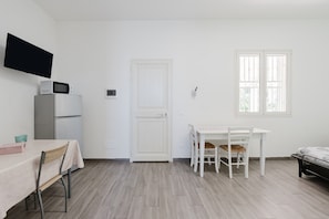 A small, clean room with a white table, chairs, a microwave, a refrigerator, and a door.