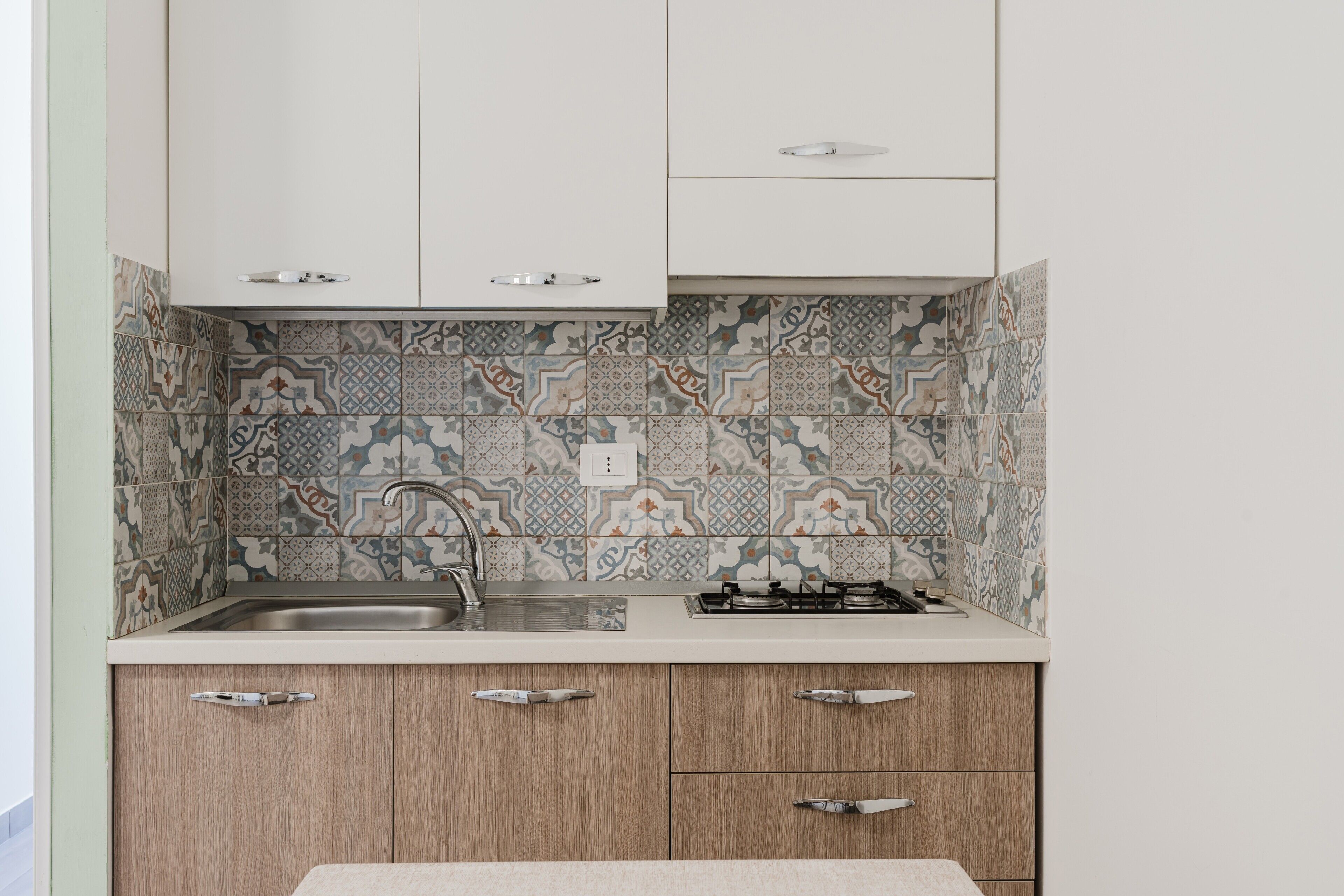 A kitchen with patterned tiles, a stainless steel sink, and wooden cabinets.