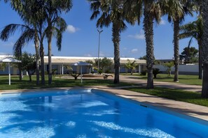 A swimming pool with palm trees, a covered patio, and a building in the background.
