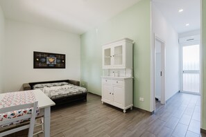 A bedroom with a bed, a white cabinet, a table with a patterned tablecloth, and a wall-mounted picture.