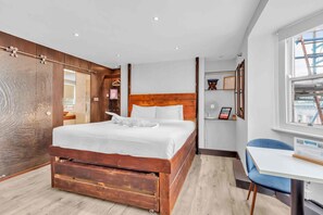 A modern hotel room with a wooden bed, a white desk, and a large window. - Grafton Copper | By My Getaways (Brighton)