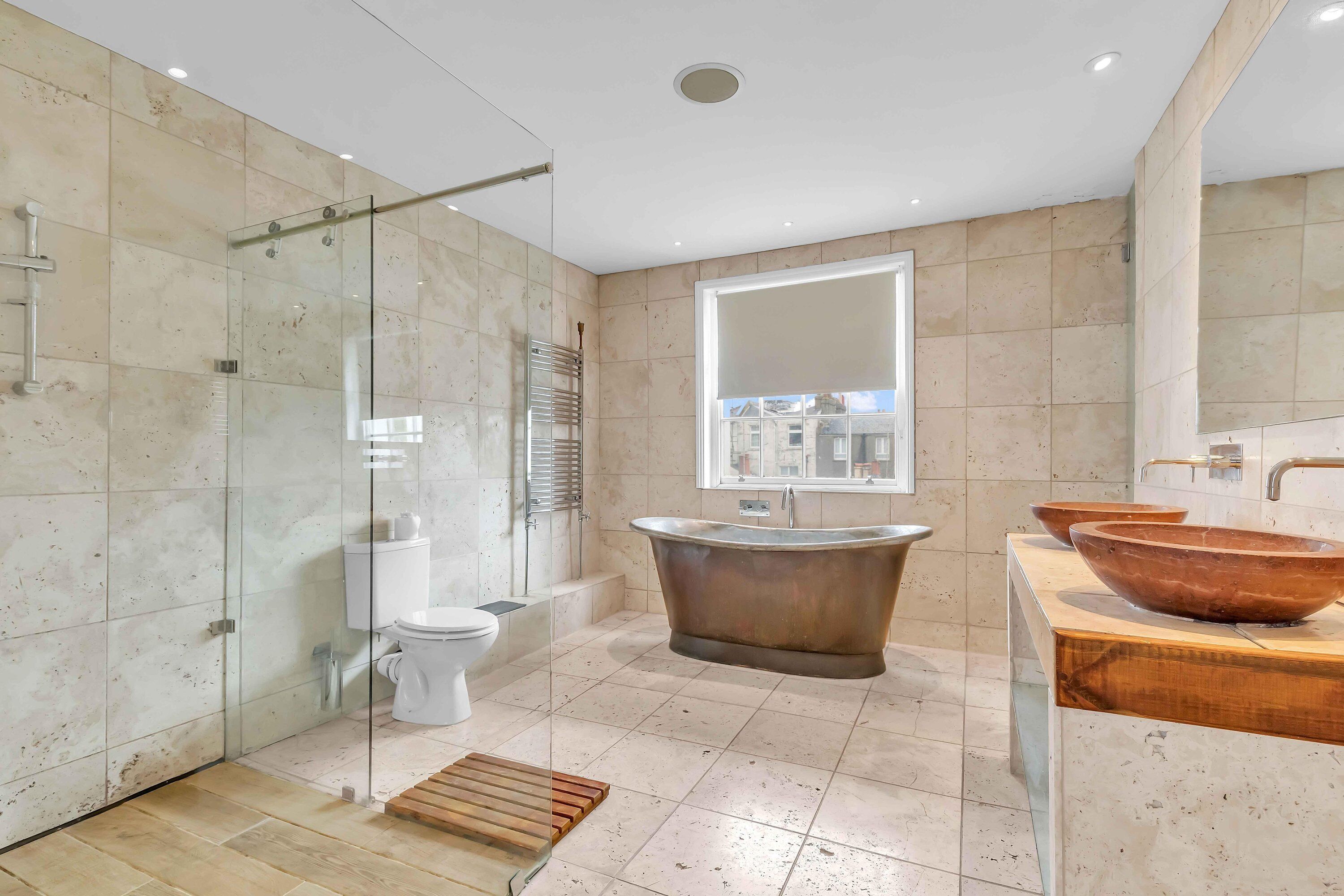 A modern bathroom with a glass-enclosed shower, a freestanding bathtub, a toilet, and a vanity with a large mirror and two wooden bowls.
