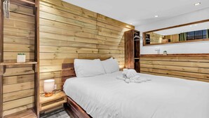 A hotel room with a wooden panel wall, a bed with white bedding, a bedside table with a lamp, and a mirror above the bed. - Grafton Woodshack | By My Getaways (Brighton)