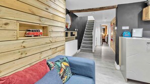 A modern interior with a wooden wall, a blue sofa, a red and white toy van, and a staircase leading to another room. - Grafton Woodshack | By My Getaways (Brighton)