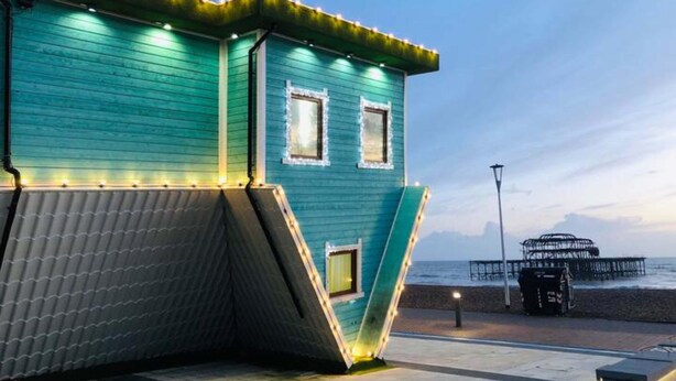 A teal building with a slanted roof, two windows, and a railing with lights. - Grafton Woodshack | By My Getaways (Brighton)