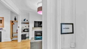 A modern living room with a grey sofa, wooden flooring, and a fireplace. There is a shelf with various items and a framed picture on the wall. - Grafton Driftwood | By My Getaways (Brighton)