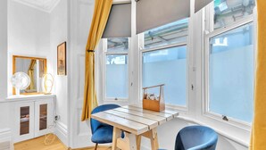 A room with a wooden table, two blue chairs, a mirror, and a window with a view. - Grafton Driftwood | By My Getaways (Brighton)