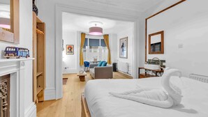 A hotel room with a large bed, a wooden floor, a desk with a chair, a small table, and a window with curtains. - Grafton Driftwood | By My Getaways (Brighton)