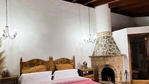 A bedroom with a wooden ceiling, a stone fireplace, and a bed with white and pink bedding.