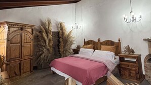 A rustic bedroom with a wooden bed, a stone wall, and a chandelier.