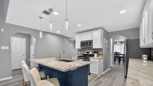 A modern kitchen with a central island, white cabinetry, stainless steel appliances, and pendant lighting.
