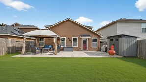 A residential backyard with a covered patio, a barbecue grill, and a shed.