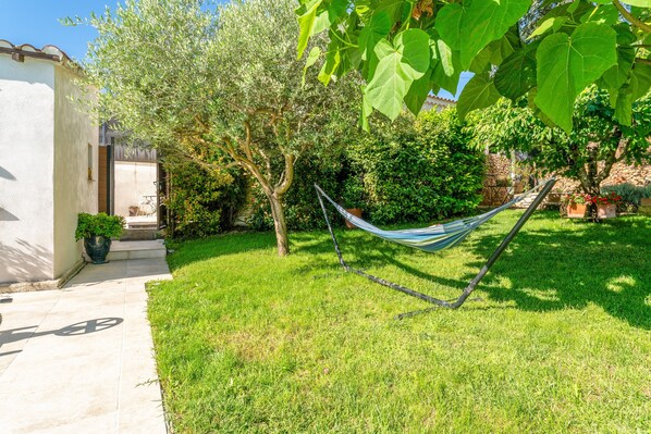 Un jardin avec un hamac, un sentier et un bâtiment doté d’une porte.