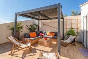 A covered outdoor seating area with wicker furniture, a cushioned sofa, and potted plants.