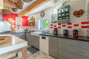 Une cuisine avec un mur rouge, des carreaux blancs, un lave-vaisselle et une machine à café.