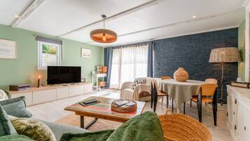 Un salon comprenant un téléviseur, un canapé, une table basse et un coin repas avec des chaises et une table.