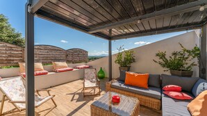 Eine Terrasss mit Korbmöbeln, einem Glastisch und Blick auf die Landschaft.