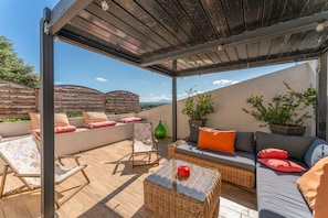 An outdoor patio with wicker furniture, a glass table, and a view of the landscape.
