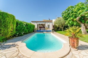 Une piscine avec une terrasse carrelée, un bâtiment doté d’un toit en tuiles et une plante en pot.