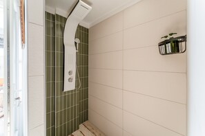 Une salle de bain avec une douche, des murs recouverts de carreaux verts, une porte blanche et une étagère contenant des articles de toilette.