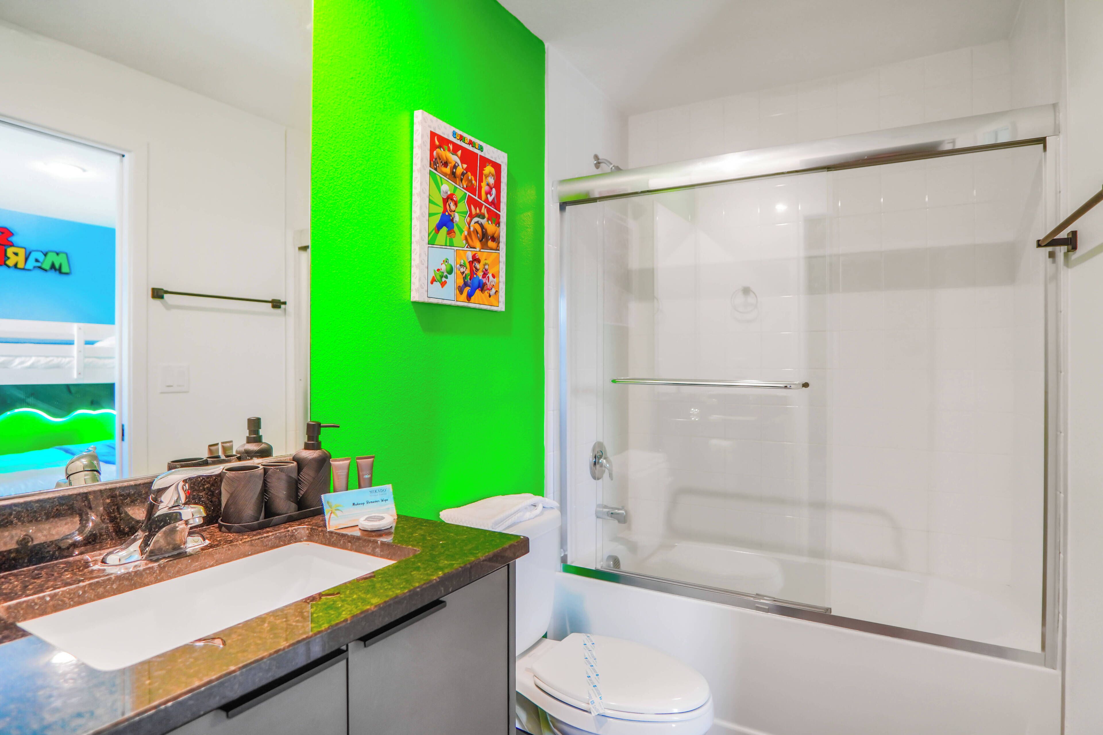 Un baño con una pared de acento verde, una ducha con puerta de cristal y un lavabo con encimera de mármol.