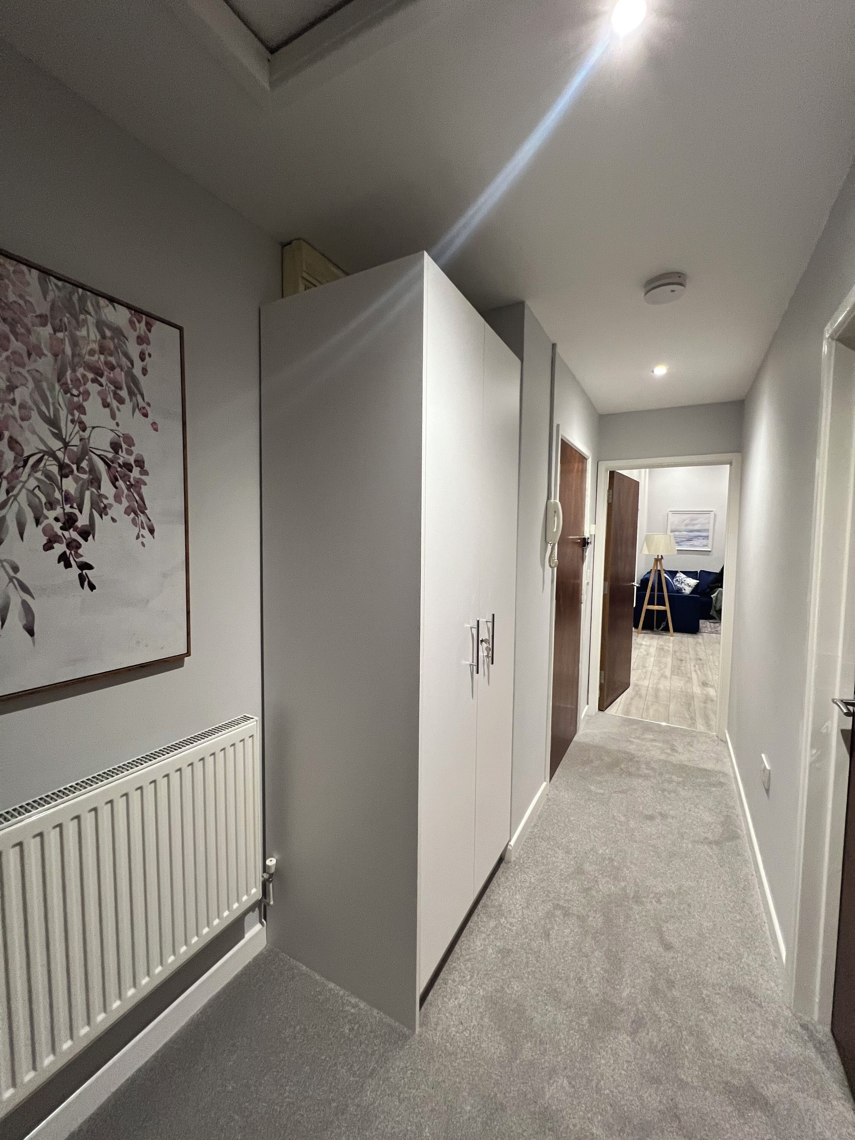 A hallway with a radiator, a white wardrobe, and a door leading to another room.