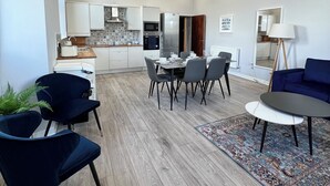 Un salon moderne avec un coin repas, une cuisine à l’arrière-plan et un canapé bleu.