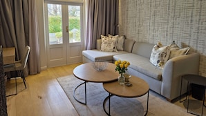 Un salon moderne avec un canapé, une table basse et une table à manger. Il y a une grande fenêtre avec des rideaux, un mur à motifs et une porte donnant sur l’extérieur.