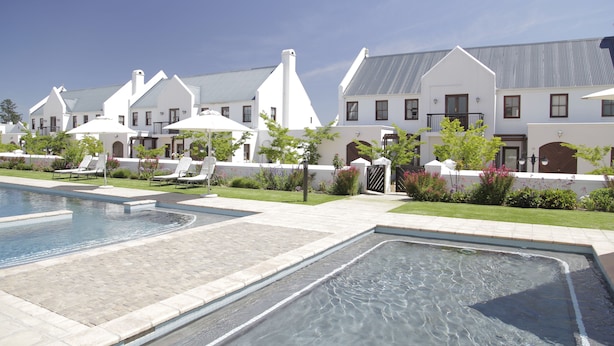 Un espace piscine offrant une vue dégagée sur les bâtiments environnants, notamment une grande maison blanche avec un toit en pente et une maison plus petite avec un toit plat.