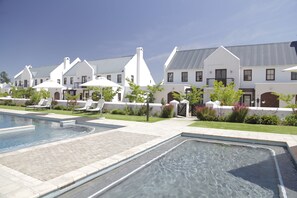 Un espace piscine offrant une vue dégagée sur les bâtiments environnants, notamment une grande maison blanche avec un toit en pente et une maison plus petite avec un toit plat.