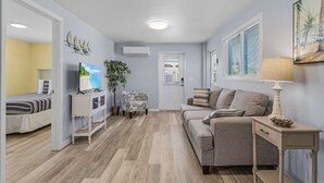 A living room with a sofa, a TV, a side table, and a door leading to another room.