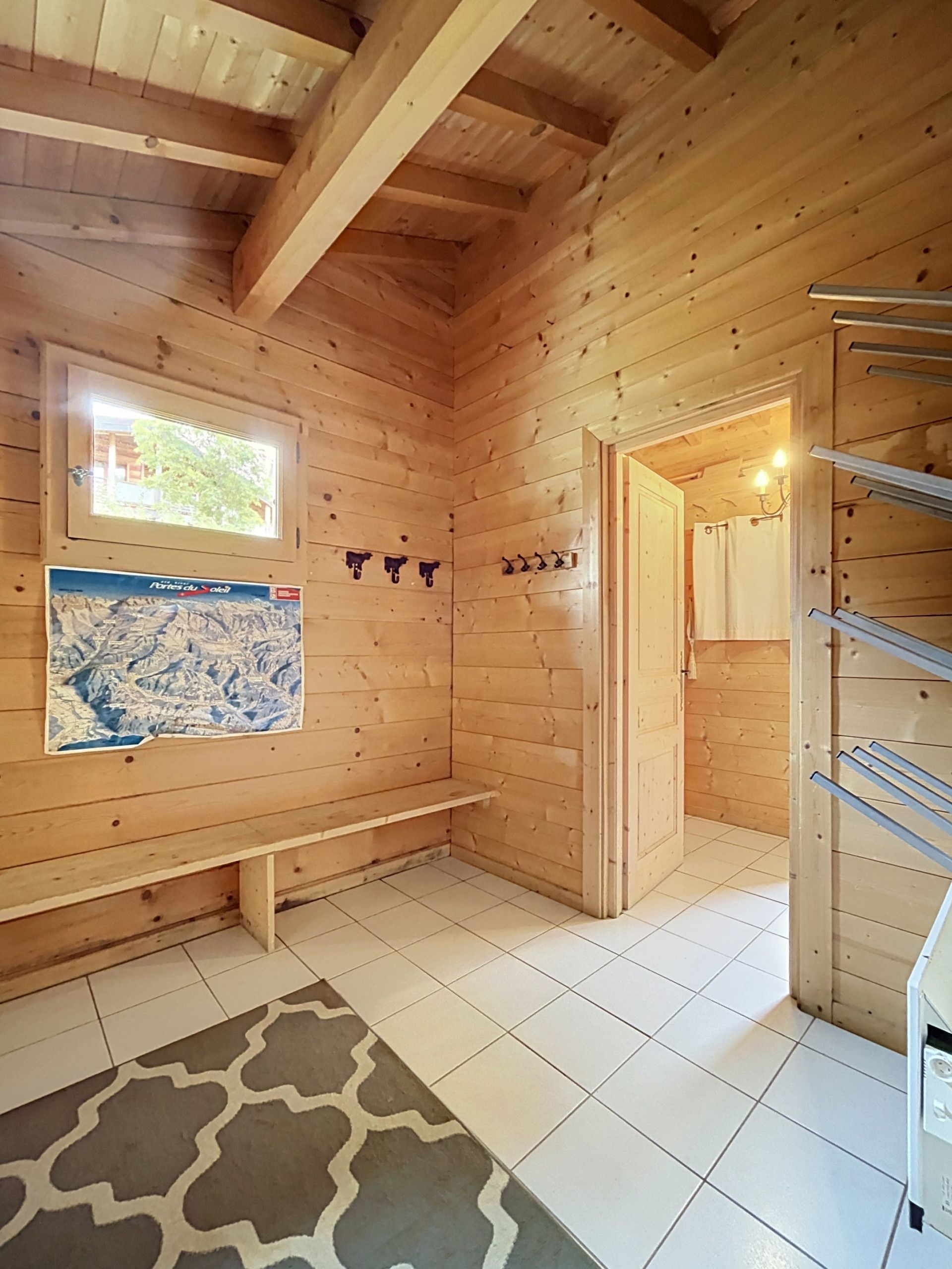 Ein Holzblockhaus-Interieur mit Fliesenboden, einer Bank, einem Fenster mit Blick und einer Tür zu einem anderen Raum.