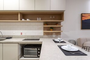 A modern kitchen with a built-in oven, a dining area with a table set for two, and a wall-mounted shelf with decorative items.