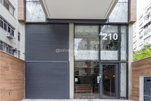 Une entrée moderne, avec une grande porte en verre, le numéro 210, et un banc en bois à l’extérieur.