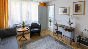 A living room with a sofa, a chair, a small table with a plant, a desk with a lamp, and framed pictures on the wall. - Apartment 'Topas' with Wi-Fi (Freiburg im Breisgau)