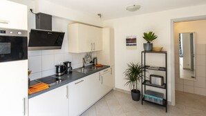 A modern kitchen with white cabinets, a black countertop, a built-in oven, and a black range hood. - Apartment 'Topas' with Wi-Fi (Freiburg im Breisgau)